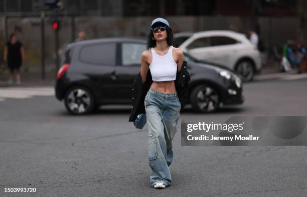 Xiayan Guo is wearing a denim blue cap from Lovechild 1979, large black sunglasses, a cropped white tank top, wide low waist denim pants in used...