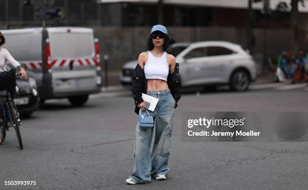 Xiayan Guo is wearing a denim blue cap from Lovechild 1979, large black sunglasses, a cropped white tank top, wide low waist denim pants in used...