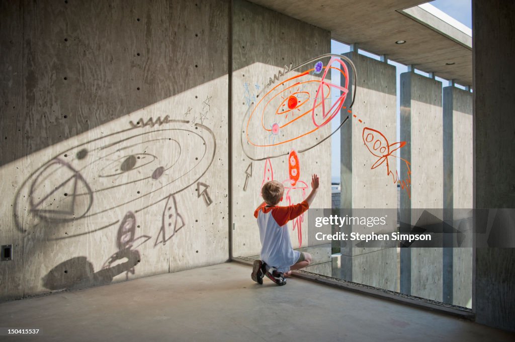 Boy drawing rocket ships and planets on window