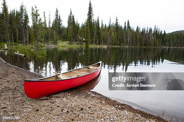 red canoe on the shore of a lake. - bend oregon stock pictures, royalty-free photos & images