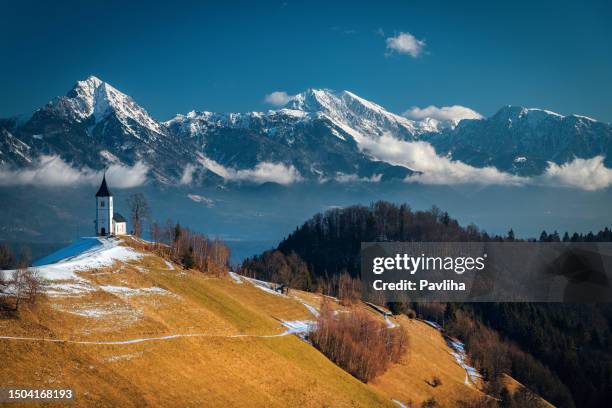 vista panorámica del hermoso paisaje de montaña del país de las maravillas de invierno en los alpes con la iglesia de peregrinación de jamnik y los famosos alpes julianos en el fondo, eslovenia tiempo de navidad en europa - ipomoea fotografías e imágenes de stock