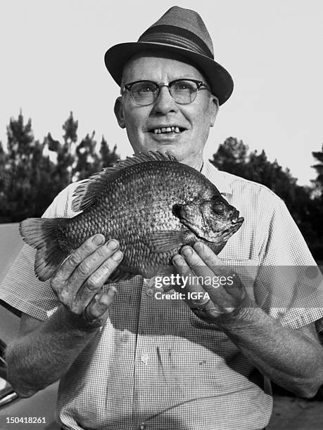 Man stands holding a 2 pound 6 ounce bluegill caught using 10 pound line on May 15, 1965.