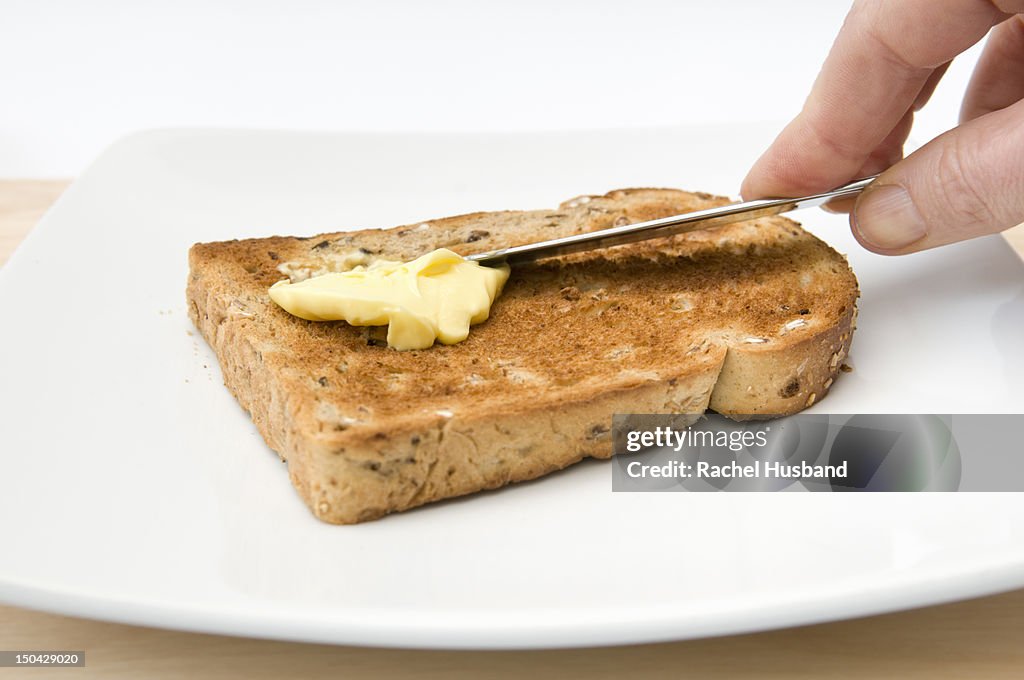 Hand buttering a piece of granary toast