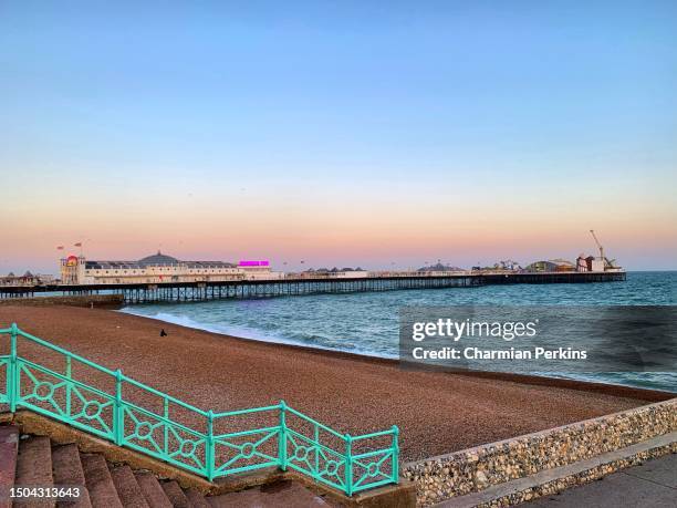 brighton palace pier at sunset with sea and pebble beach in foreground under dramatic beautiful evening sky at dusk in brighton in sussex, uk in june 2022 - fairground stall stock pictures, royalty-free photos & images