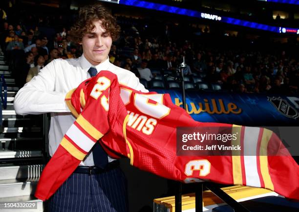 Aydar Suniev puts on a jersey after being selected 80th overall by the Calgary Flames during the 2023 Upper Deck NHL Draft - Rounds 2-7 at...