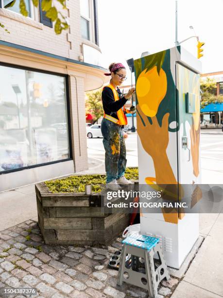 young latin woman artist painting sidewalk box mural - art and craft equipment stock pictures, royalty-free photos & images