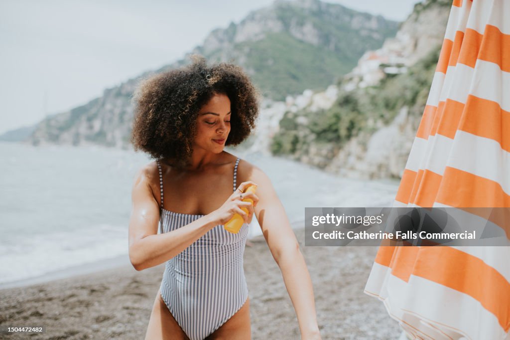 A woman spritzes her arm with spray sun screen at the beach