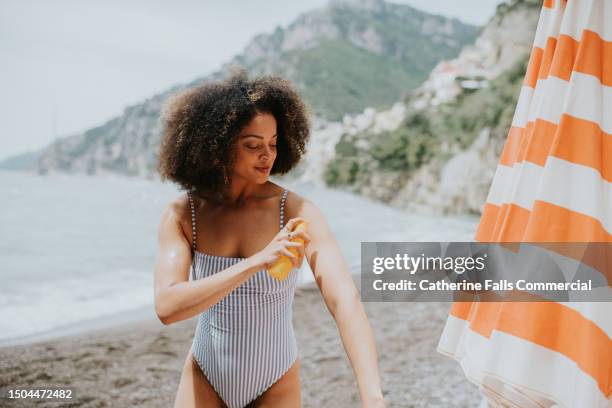 a woman spritzes her arm with spray sun screen at the beach - aplicar imagens e fotografias de stock