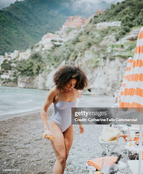 a woman spritzes her leg with spray sun screen at the beach - sun tan stock pictures, royalty-free photos & images