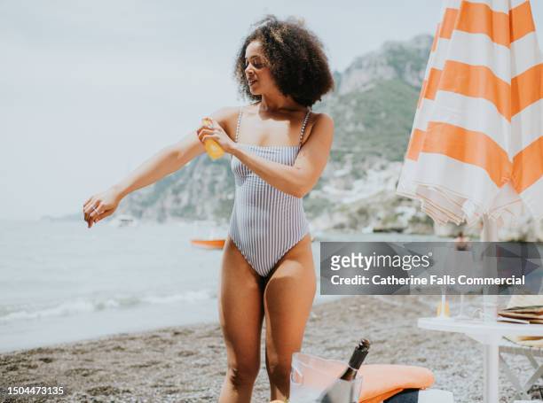 a woman spritzes her arm with spray sun screen at the beach - sunburn tourist stock-fotos und bilder
