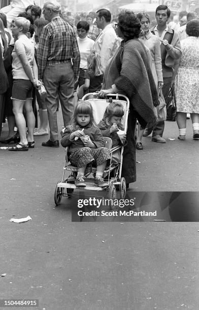 Two children sitting in a dual stroller eat snow cones as a woman stands behind them on Mott Street during the Feast of St Anthony of Padua Festival,...