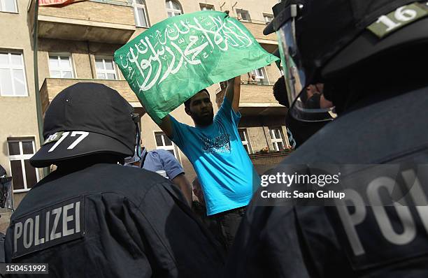 Riot police watch as a protester waves a flag with Arabic written on it while demonstrators protest the arrival of supporters of the pro Deutschland...