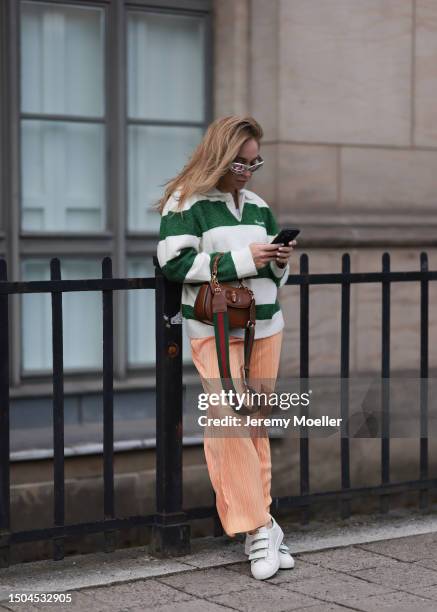 Sonia Lyson wearing Copenhagen Studios white and green sneaker, Storets orange pleated pants, Axel Arigato striped Creme beige and green long sleeve...