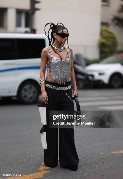 Fashion Week guest is wearing large black sunglasses from Balenciaga, two large necklaces in silver, a shiny silber top consisting of tear tabs of...