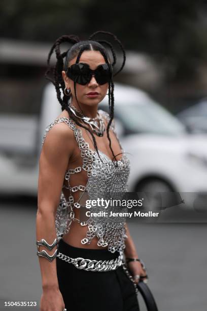 Fashion Week guest is wearing large black sunglasses from Balenciaga, two large necklaces in silver, a shiny silber top consisting of tear tabs of...