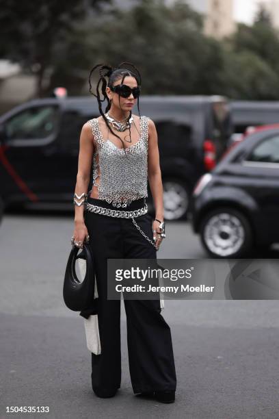Fashion Week guest is wearing large black sunglasses from Balenciaga, two large silver necklaces, a shiny silver top consisting of can tabs and...