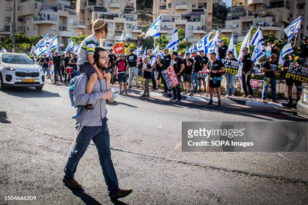 Jewish religious man takes his son on his shoulders as he walks past an Anti reform protest. Over 200 protesters against the government's judicial...
