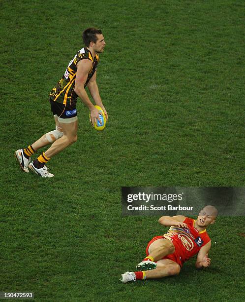 Luke Hodge of the Hawks looks to kick the ball as Gary Ablett of the Suns lies on the ground during the round 21 AFL match between the Hawthorn Hawks...