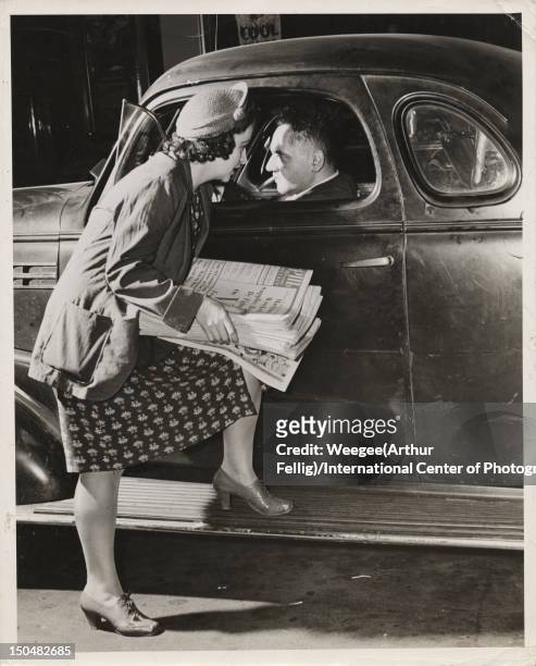Photographer and photojournalist Arthur Fellig (1899 - 1968, aka Weegee, gets a tip from a PM news seller in New York, circa 1942.