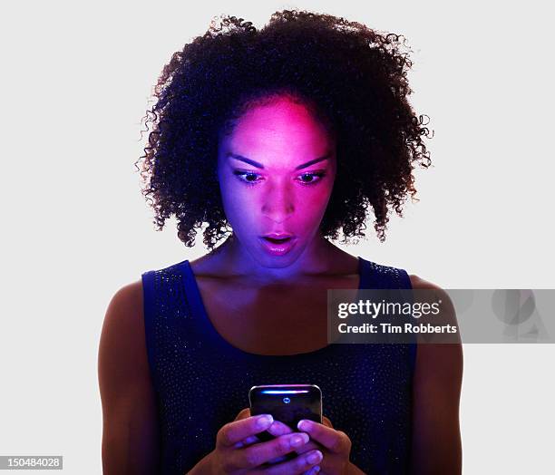 woman lit by smart phone looking surprised. - shocked woman stock pictures, royalty-free photos & images