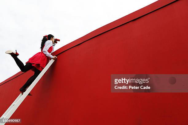 girl looking over red wall with binoculars - achtervolgen stockfoto's en -beelden