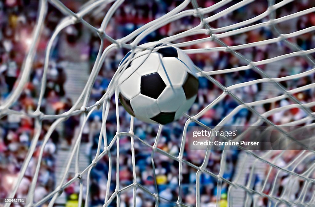 Football, or soccer ball in the back of a net