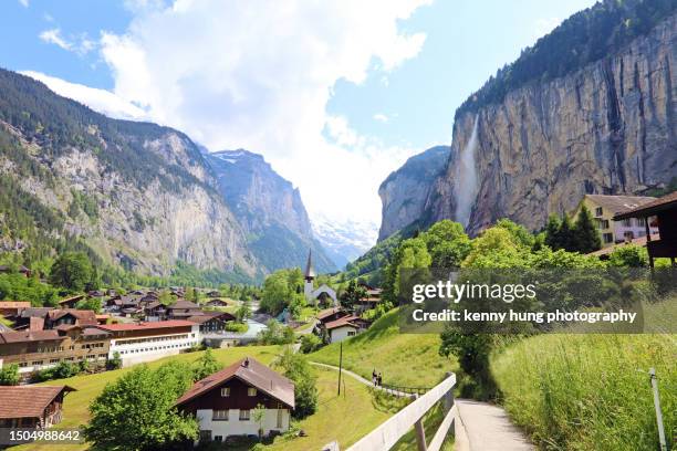 valley of lauterbrunnen with chalet-style houses amongst green fields with a backdrop of mountains and staubbach falls - lauterbrunnen photos et images de collection
