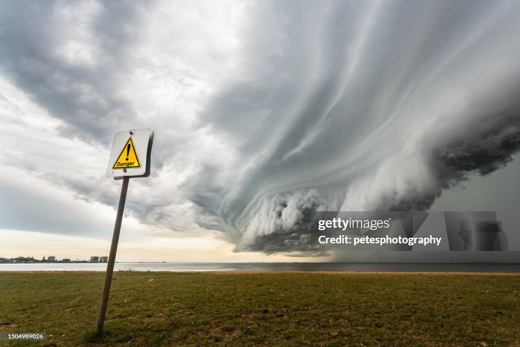 Massive shelf storm cloud with rain below over the ocean with a danger sign
