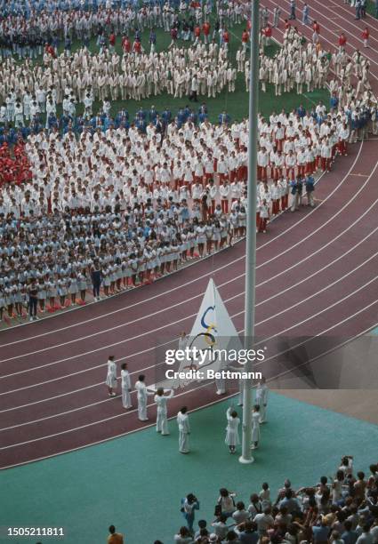 Athletes look on as the Olympic flag is raised at the Olympic Stadium in Montreal, Canada, July 17th 1976.