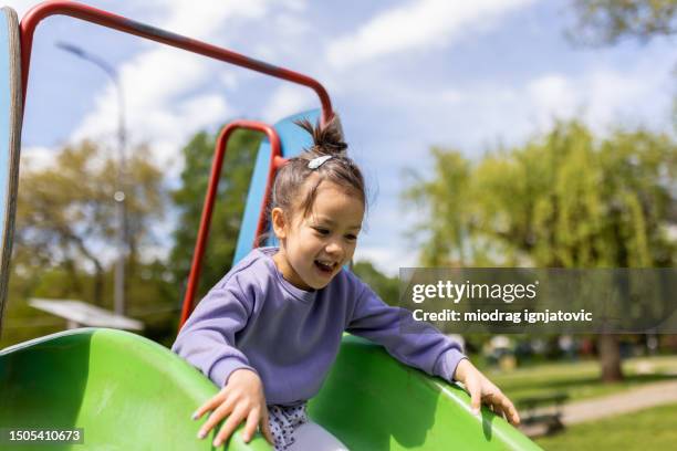 little girl playing on a slide in a public park playground - sliding stock pictures, royalty-free photos & images