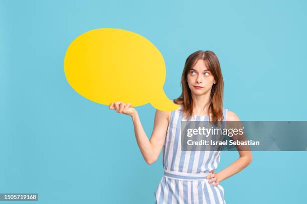 young pensive girl holding dialogue balloon on blue isolated background. - slogan stock pictures, royalty-free photos & images