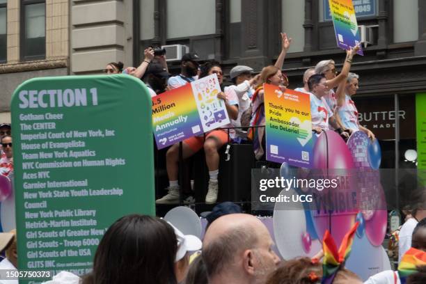 Passengers on the God's Love We Deliver float begin their journey down 5th Avenue, NYC Pride March 2023. 3 hold posters describing GLWD's work and...