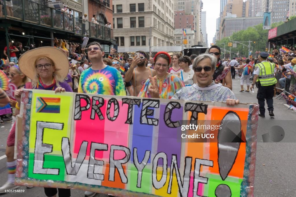 A couple carry a banner, which reads Protect Everyone, during NYC Pride March 2023