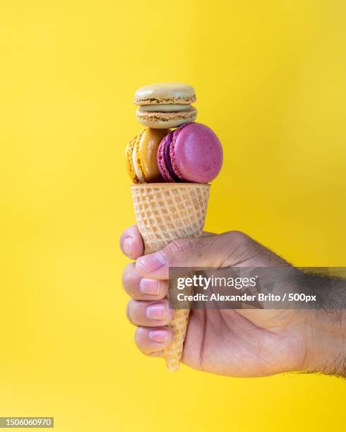 cropped hand holding ice cream cone against yellow background,naples,united states,usa - ice cream cone stockfoto's en -beelden