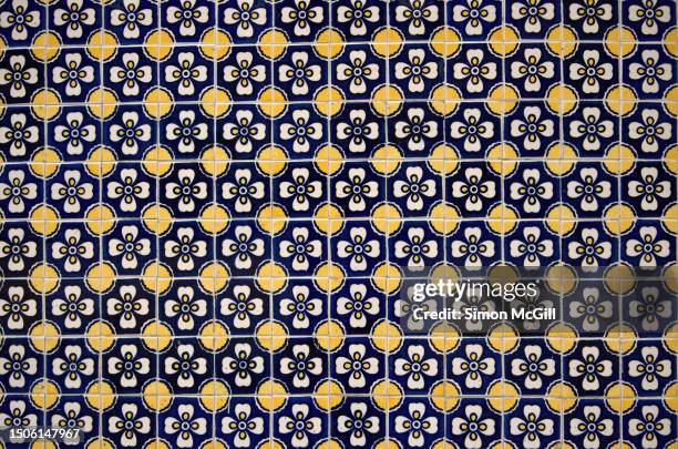hand-painted poblano talavera tiles on a building exterior wall with a repeating spot and flower in blue, white and yellow - spanish-colonial-architecture stock pictures, royalty-free photos & images