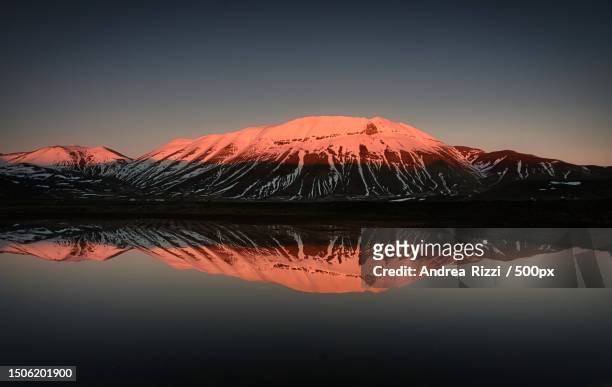 scenic view of lake by snowcapped mountains against sky during sunset,castelluccio di norcia,italy - andrea rizzi stock pictures, royalty-free photos & images