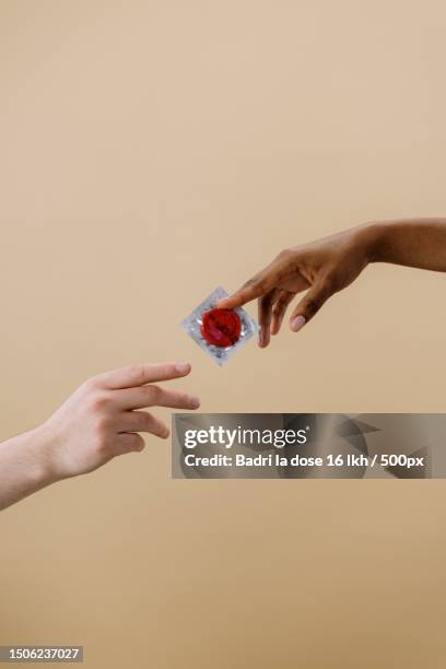 cropped hand of woman giving condom to man against brown wall,fawn creek township,kansas,united states,usa - kondome stock-fotos und bilder