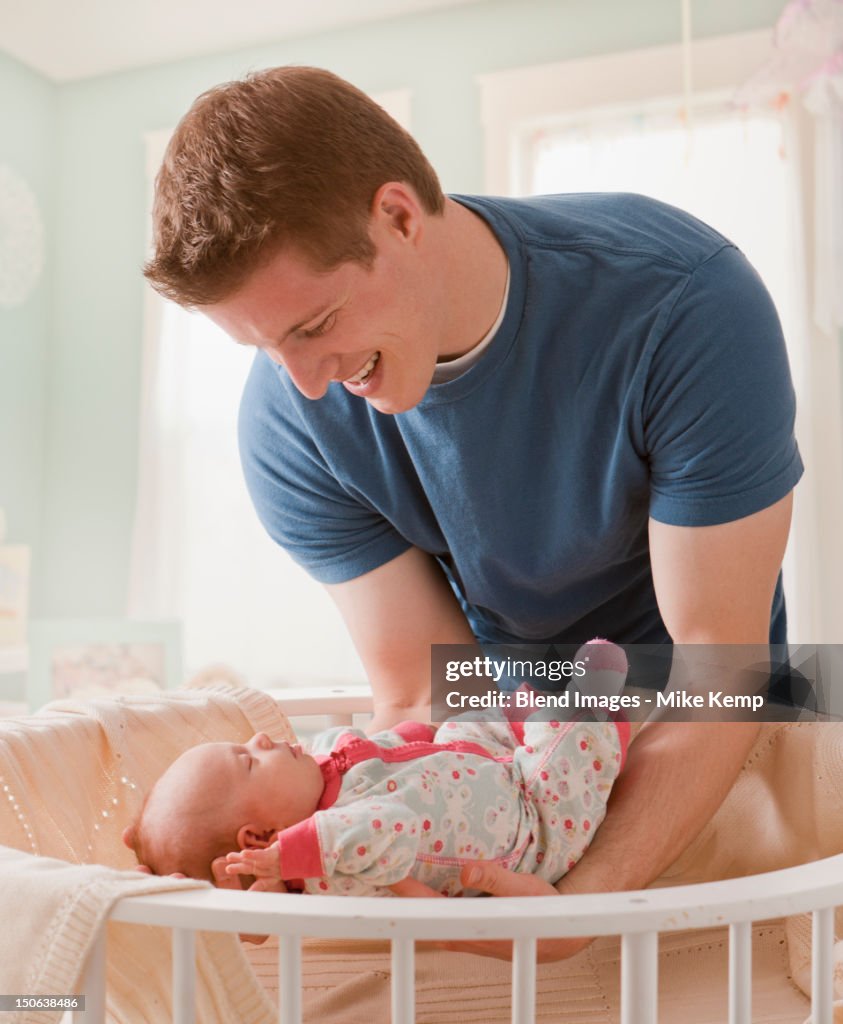 Caucasian father lifting baby girl from crib