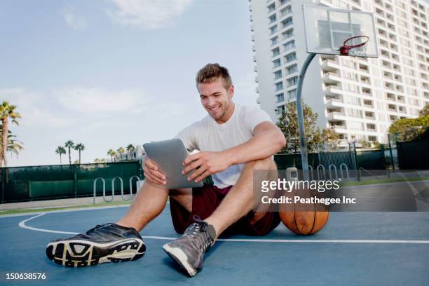 caucasian man using digital tablet on basketball court - basketball net stock-fotos und bilder