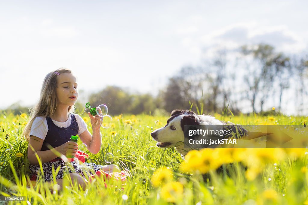 Girl blowing bubbles with dog in field