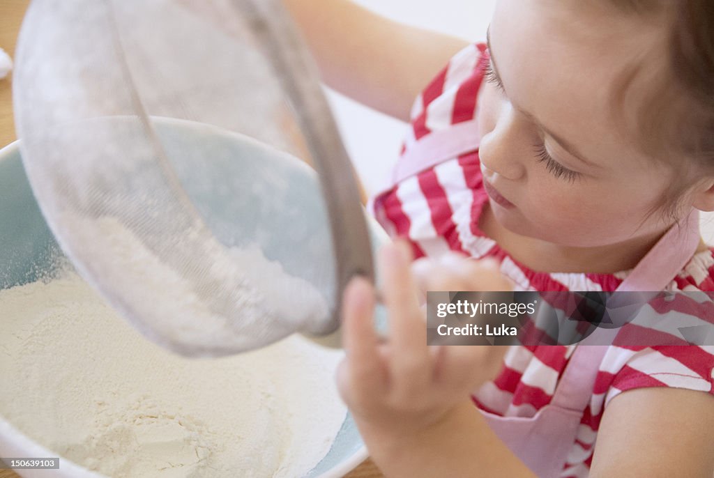 Menina Peneirar a farinha na cozinha