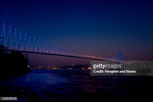 bridge over urban bay lit up at night - bosphorus bridge stock pictures, royalty-free photos & images