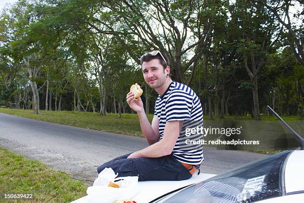 man eating sandwich on trunk of car - burger portrait photos et images de collection