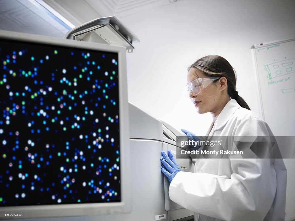 Scientist using a miccroarray to create complex strands of DNA, with a gene expression on monitor,  in biolab