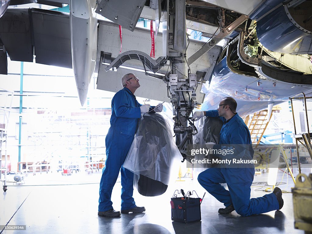 Aircraft engineers working on undercarriage area and landing gear of 737 jet plane