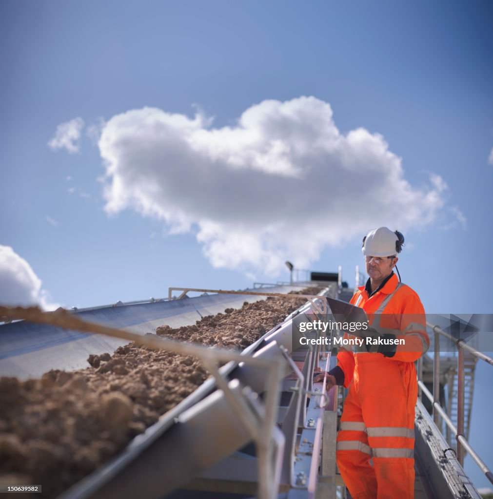 Worker inspecting stone screening and crushing machine in quarry