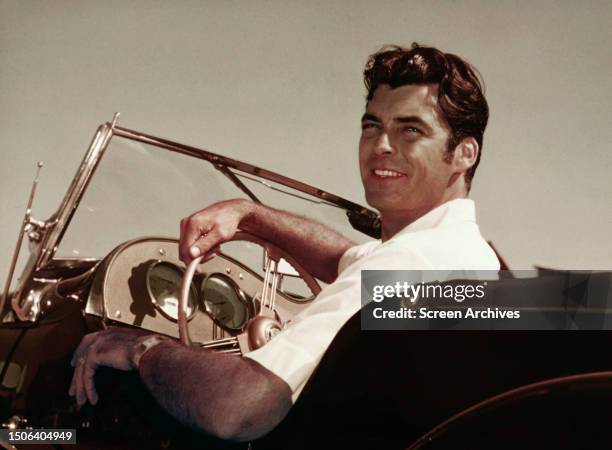 American actor Rory Calhoun smiling at the wheel of convertible sports car, circa 1953.