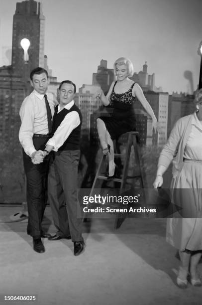 Marilyn Monroe looks on from a stepladder as Gene Kelly demonstates dancing moves with Yves Montand, during the filming of the 1960 comedy, 'Let's...