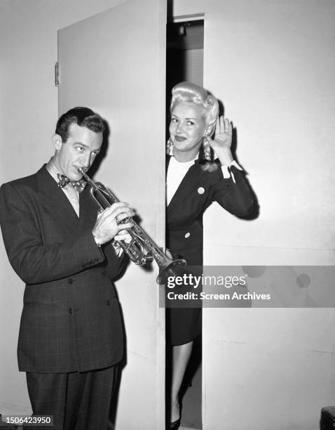 Big band leader Harry James serenading his wife Betty Grable on the trumpet at a studio stage door, circa 1944.