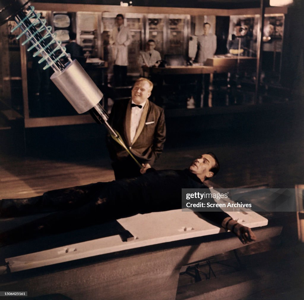 Sean Sean Connery as James Bond is tied to table as Gert Frobe watches a ...